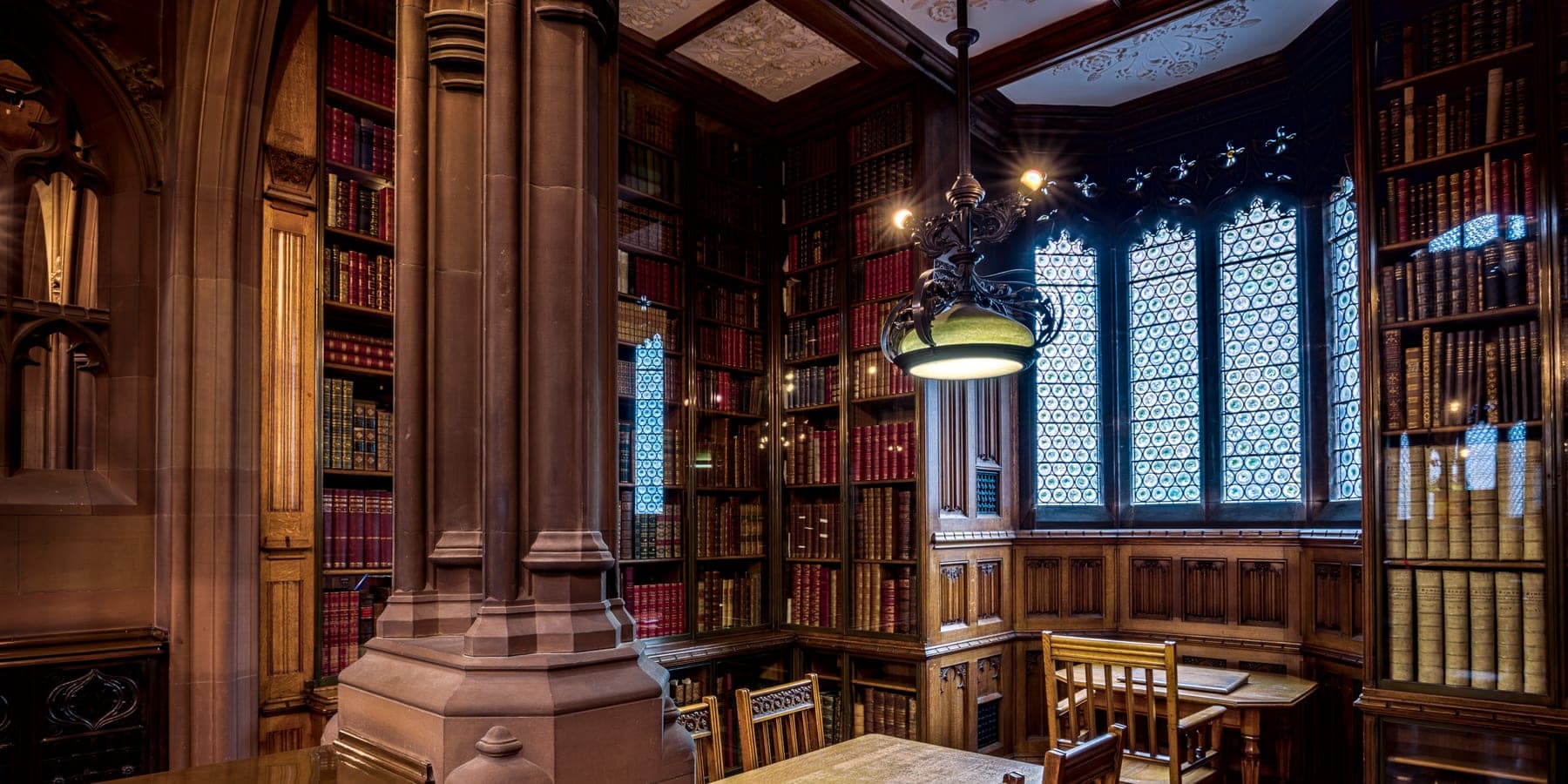 A quiet study room at the John Rylands Library in Manchester, a reading table set beneath a stained-glass window