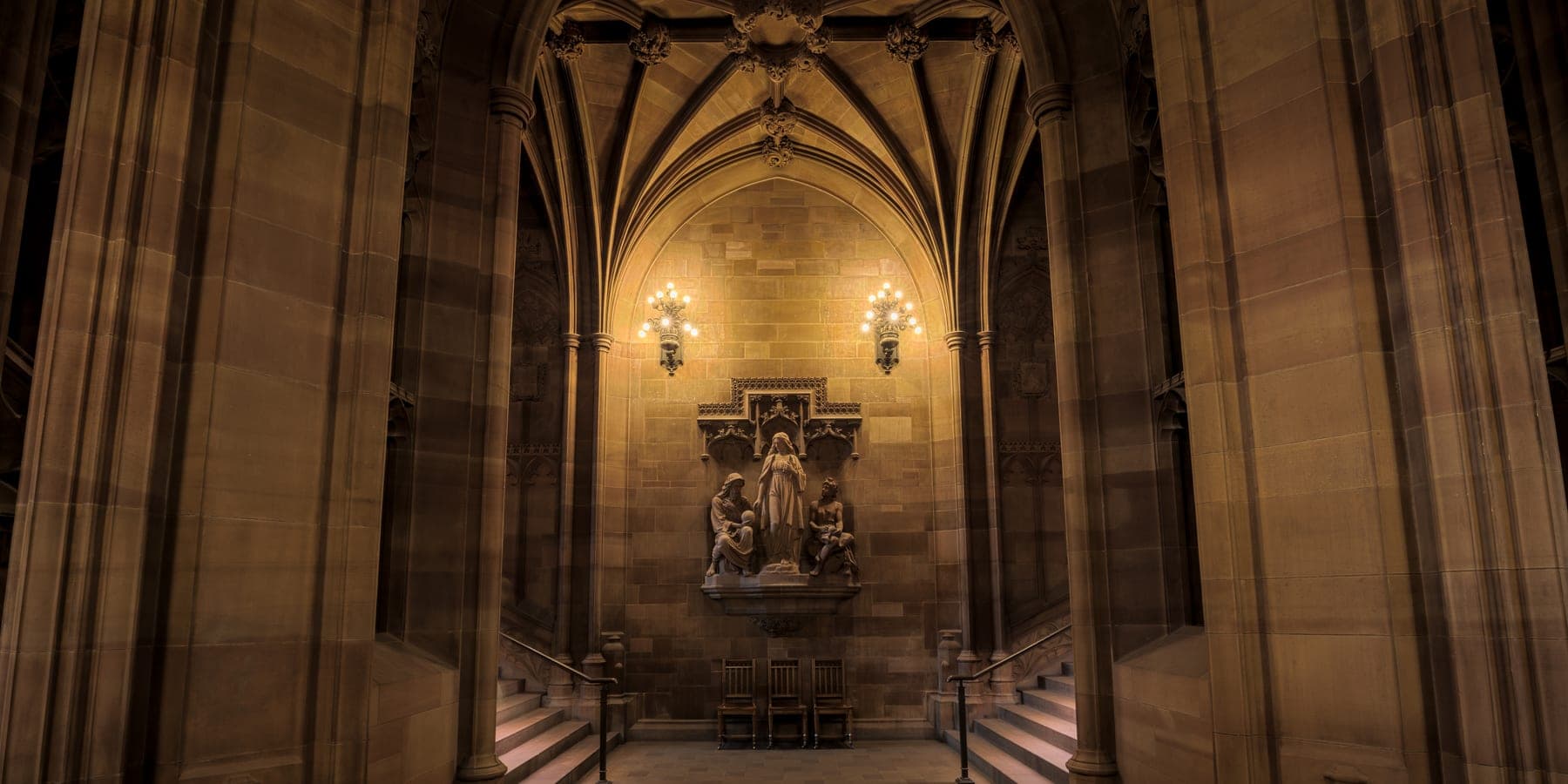The vaulted stone entrance hall of the John Rylands Library in Manchester, lit by wall lamps
